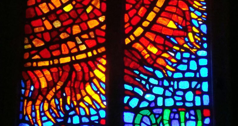 Stained glass window depicting a red/orange/yellow sun against a blue sky with Greek letters Alpha and Omega