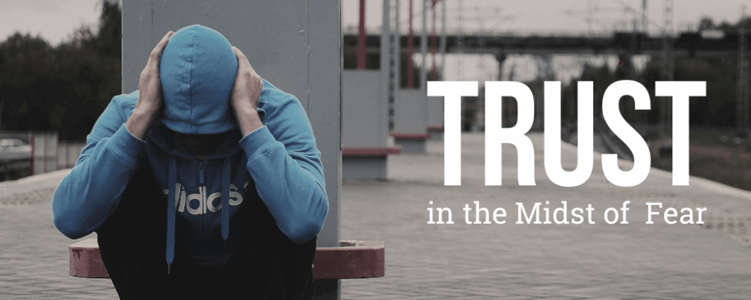 Trust in the Midst of Fear. Person in hoodie crouches on a train platform with hands over their head.