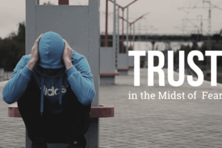 Trust in the Midst of Fear. Person in hoodie crouches on a train platform with hands over their head.